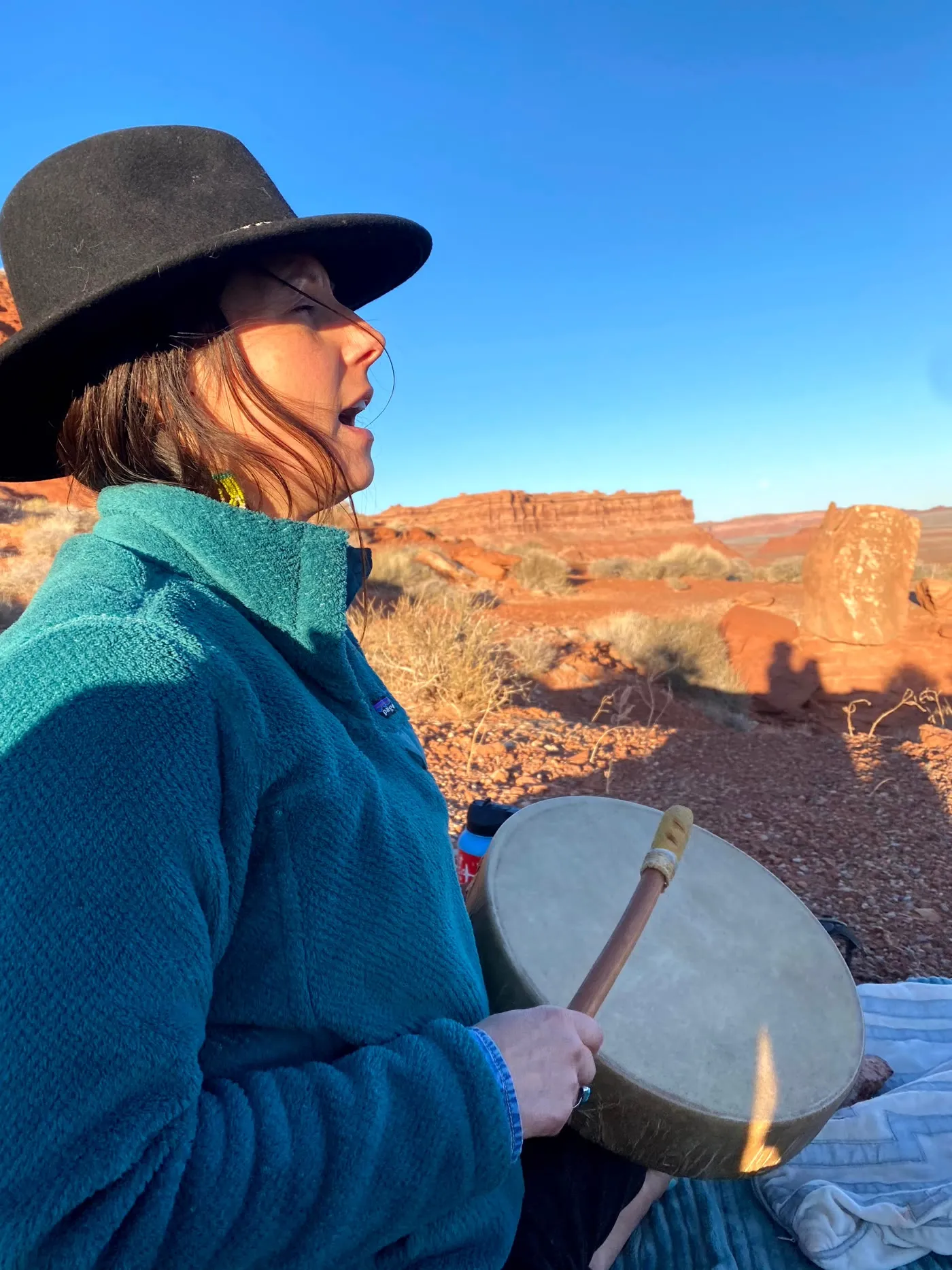 Vanessa singing and playing a hand drum in the red rock desert at golden hour.
