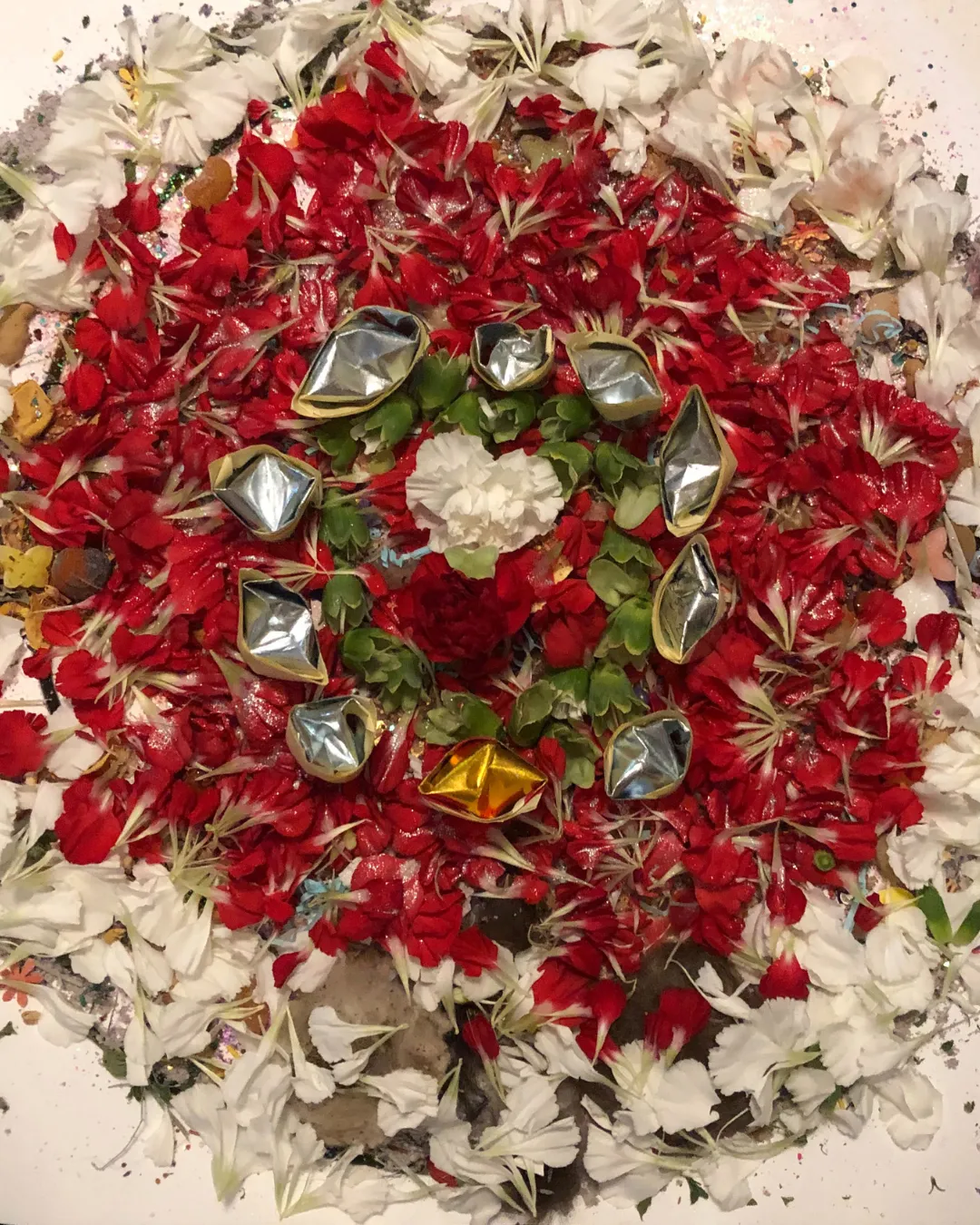 A mandala of red and white flowers ringed with small offering vessels.