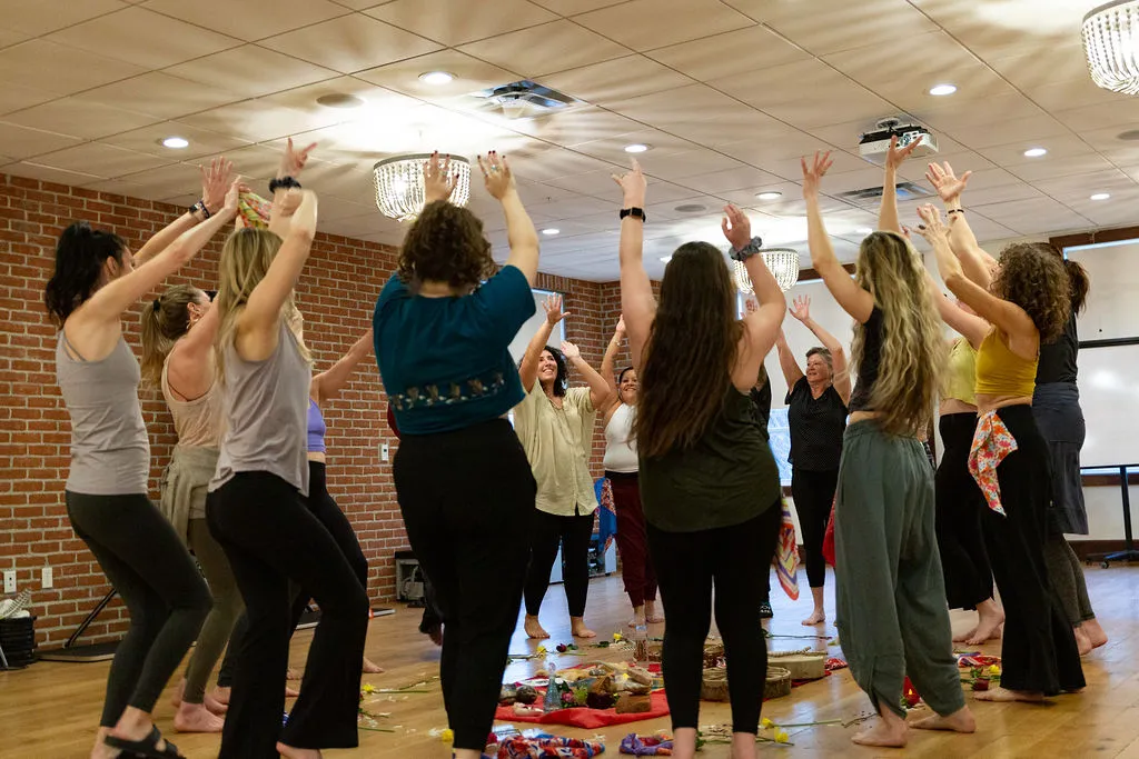 A group with arms raised in a movement circle around a floral altar.