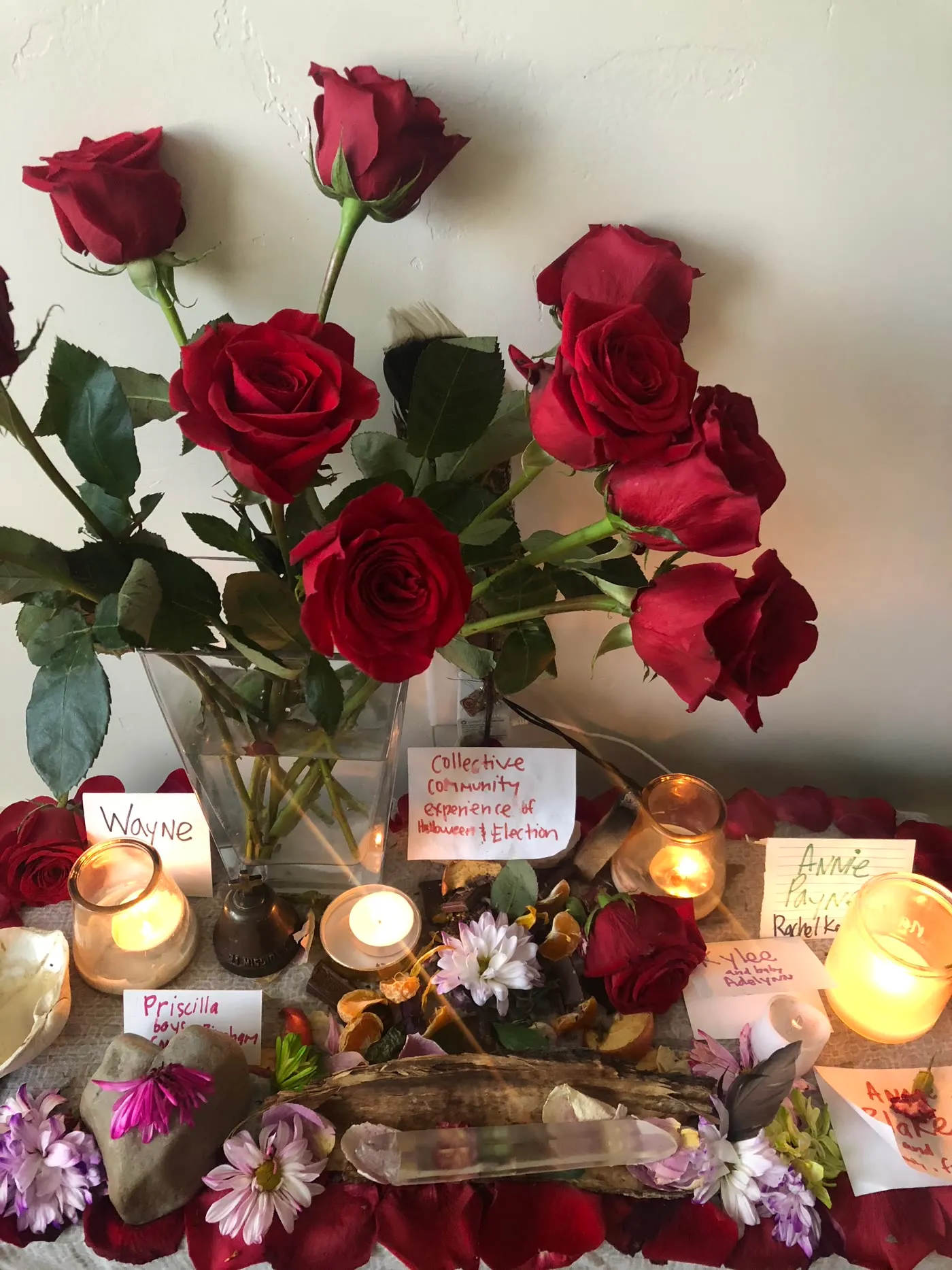 A memorial altar of red roses, candles, crystals, and handwritten name cards honoring loved ones.