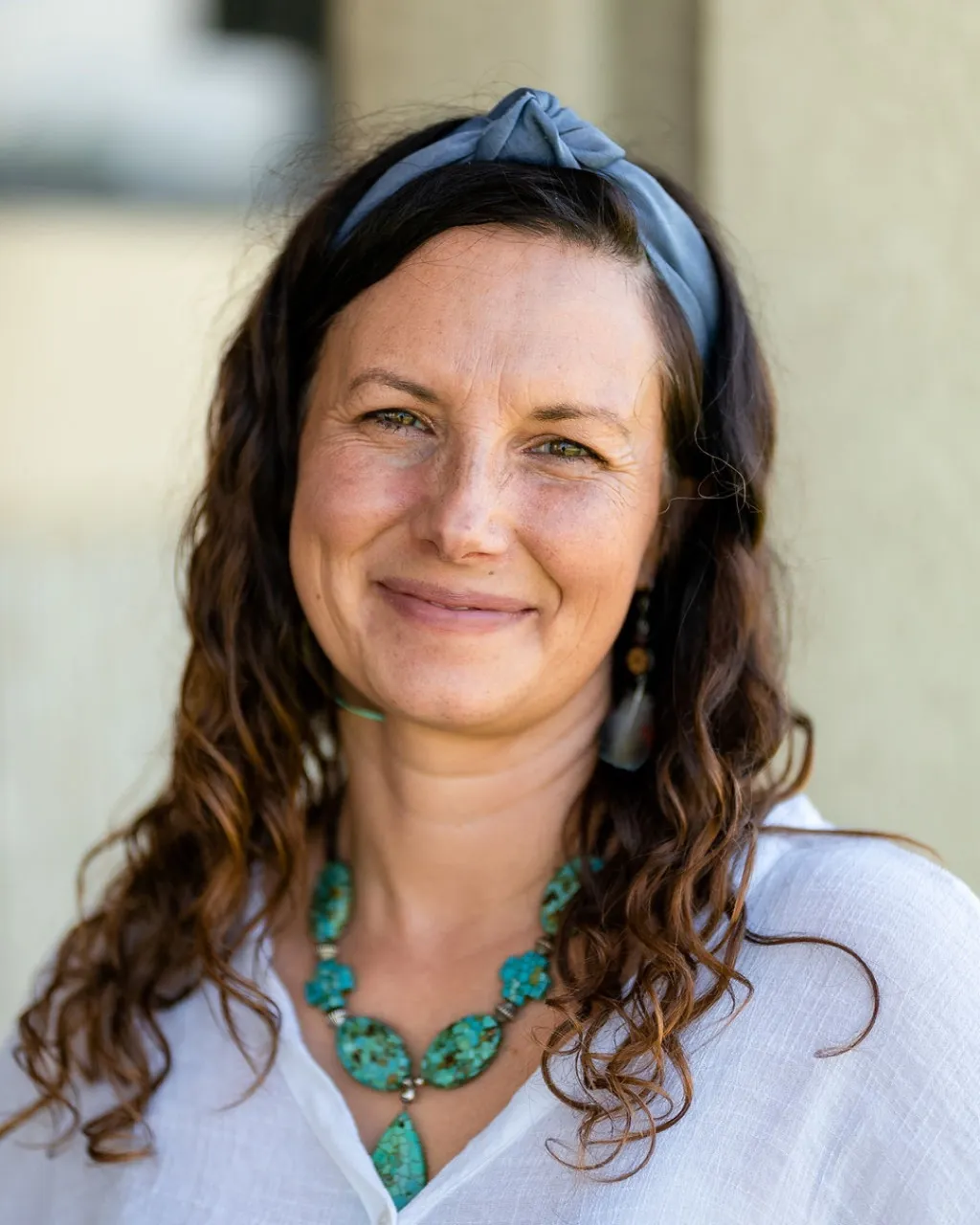 Vanessa smiling warmly, wearing a turquoise necklace and headband, a welcoming portrait.