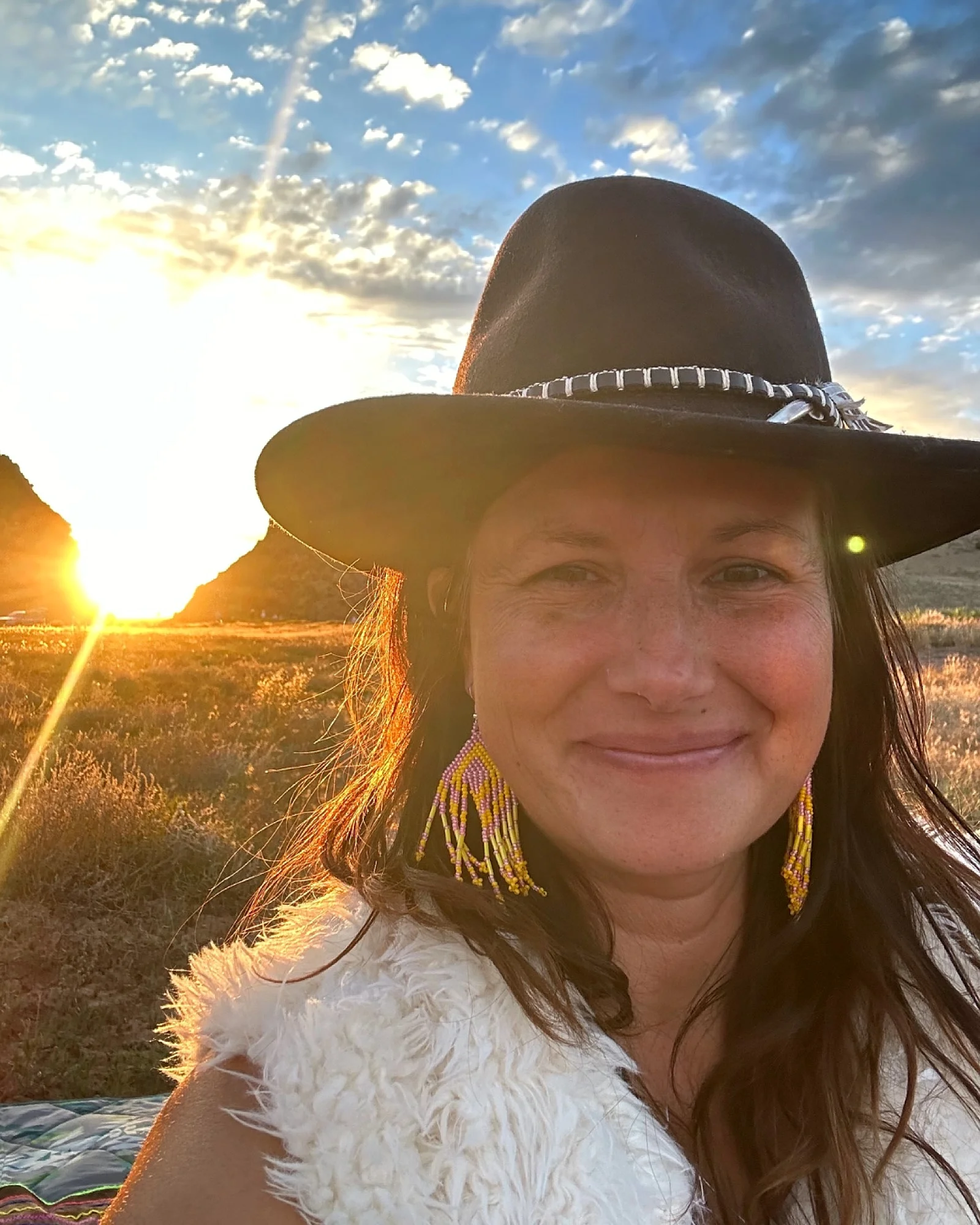 Vanessa outdoors at sunset in a wide-brimmed hat, smiling.