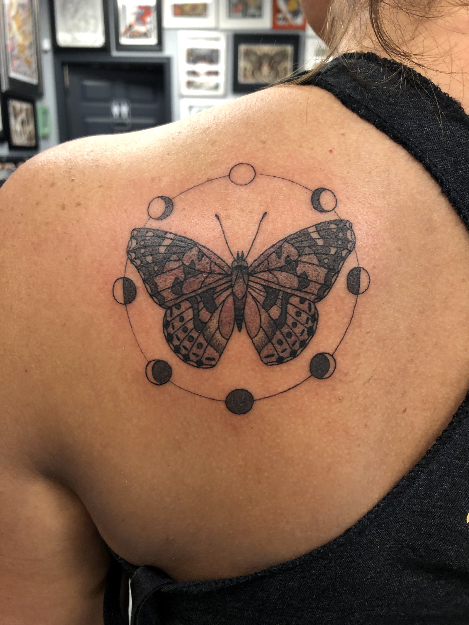 A fine-line painted lady butterfly tattooed on Vanessa's left shoulder, encircled by the eight phases of the moon.